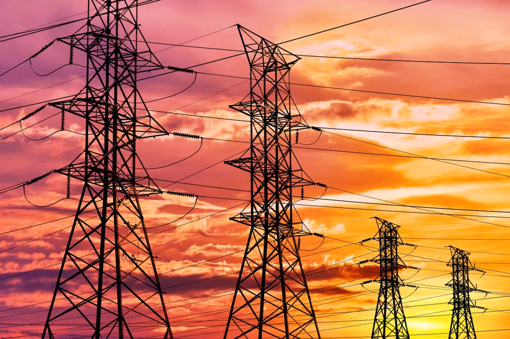 High-voltage transmission towers silhouetted against a vivid orange and pink sunset sky