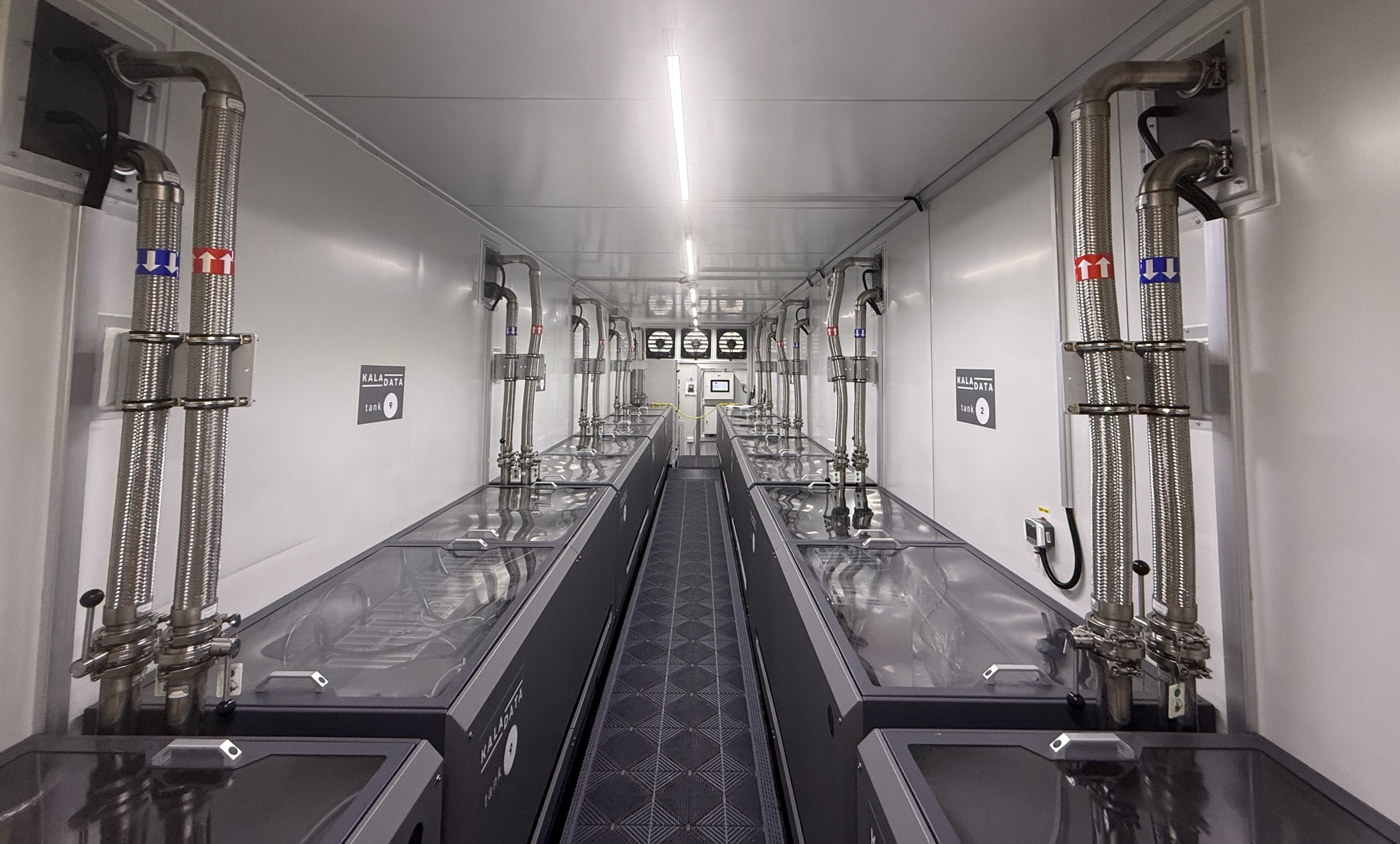 Interior of a Kala Data modular data centre container, showing rows of branded immersion cooling tanks and stainless steel pipework